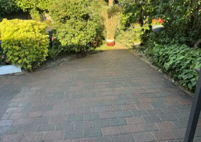 Brick pathway flanked by green foliage and hanging flower pot in a garden.