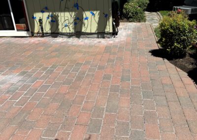 Brick pathway leading to a house with hanging plant baskets and blue wind spinners.