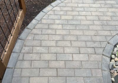 Curved brick patio path beside a wooden fence and green lawn.