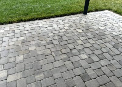 Paved area with interlocking stones next to a grass lawn and a metal post on the left edge.