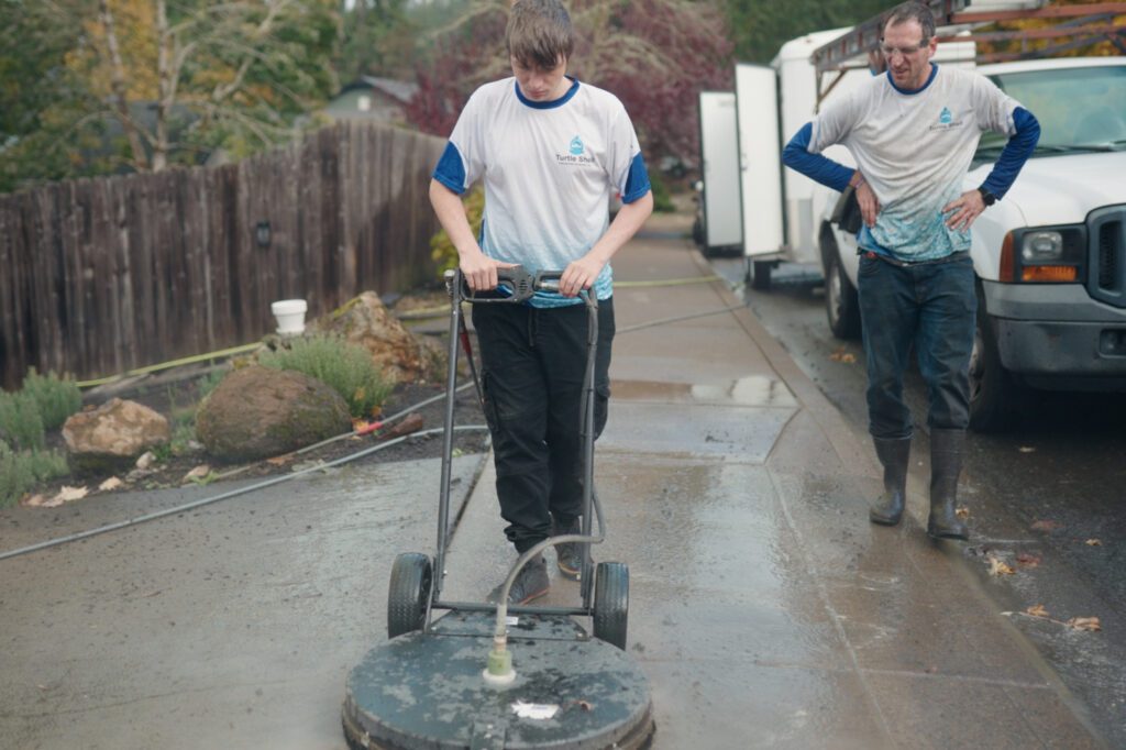 Two men power washing a driveway, removing dirt and grime for a clean and polished appearance